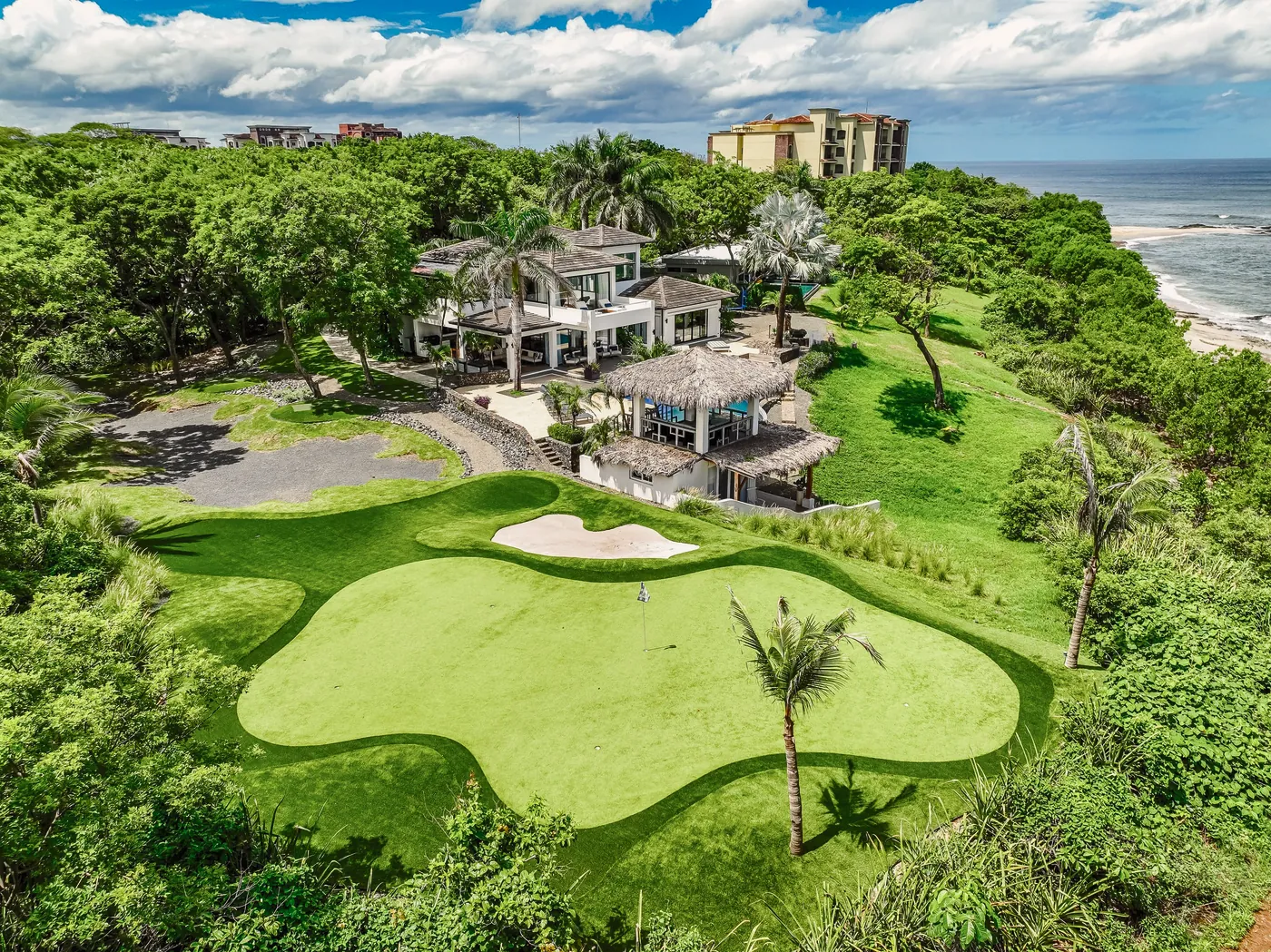 Vista aérea de un putting green, su collar y un búnker que se unen en curvas limpias sobre un acantilado