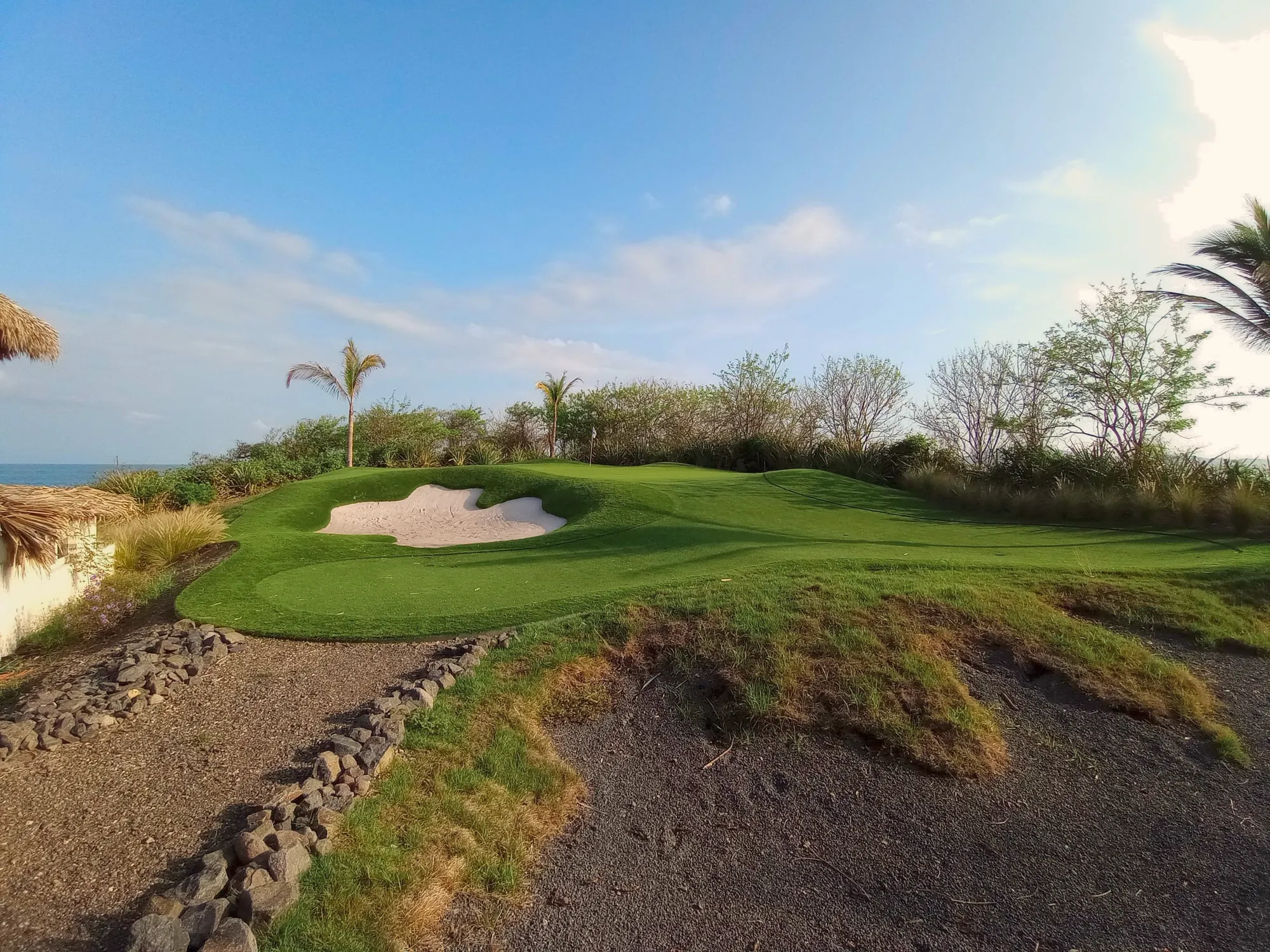 A putting green and bunker on a hillside above the sea