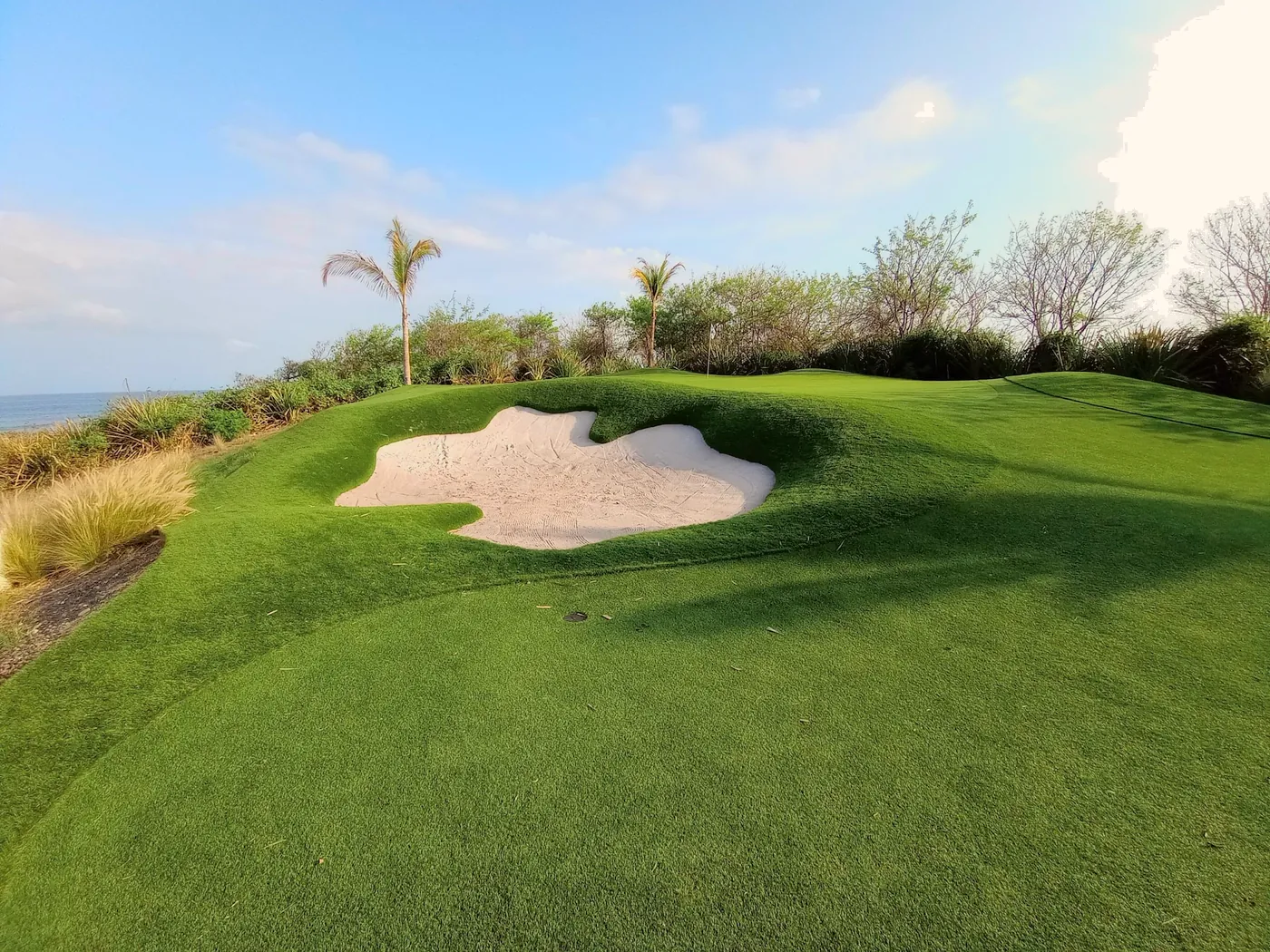 Putting green moldeado y búnker de arena con vista a la costa