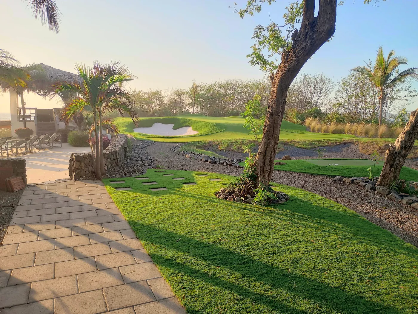 A synthetic lawn beside a stone path, with a putting green and bunker beyond