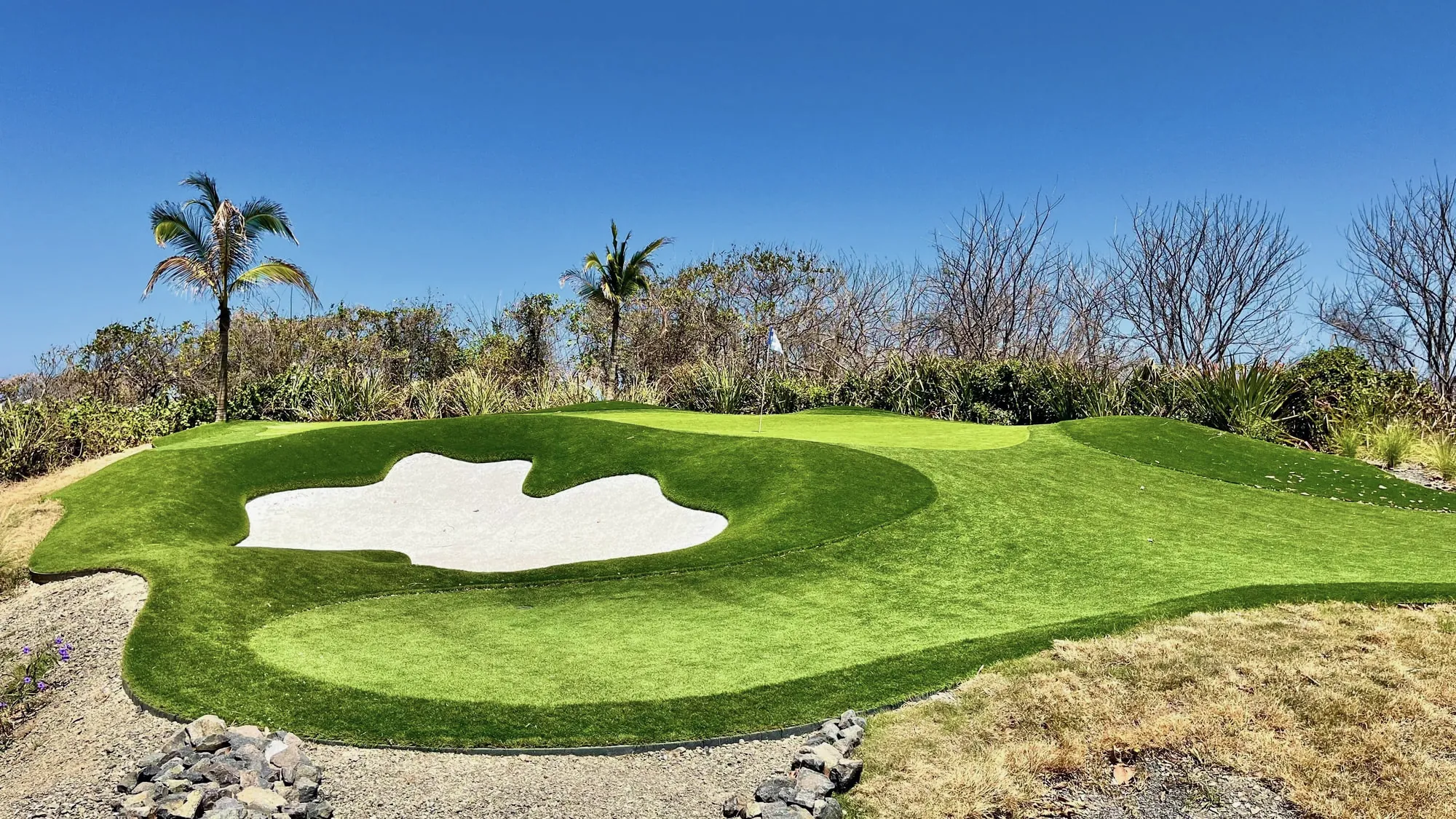 A sculpted putting green and white sand bunker under a clear blue sky
