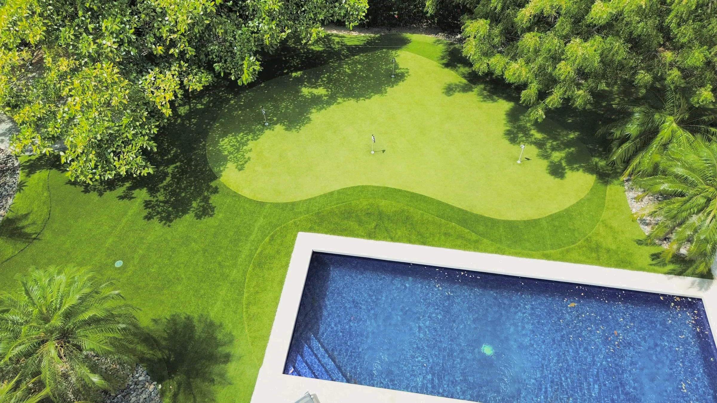 Drone view of a contoured putting green set into a lawn beside a pool