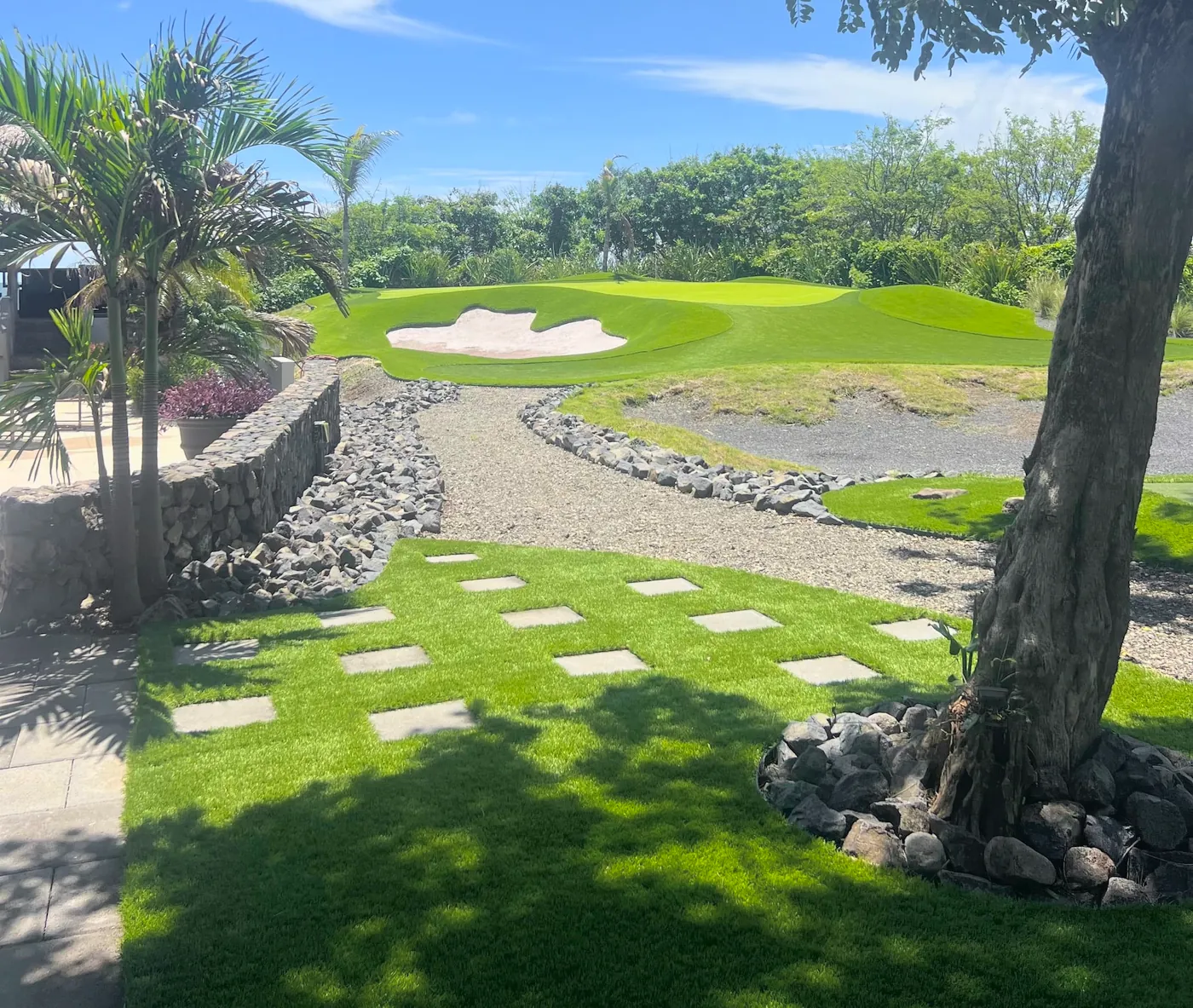 Canal de piedra de río que baja desde un putting green y lleva el agua junto al jardín