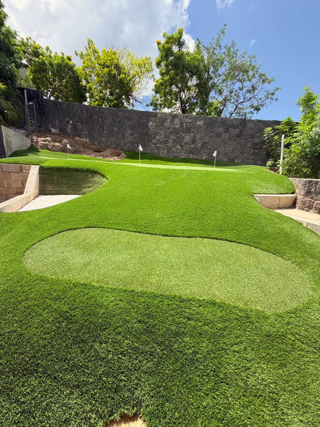 Putting green de dos niveles con búnker de arena, en un jardín rodeado de muros