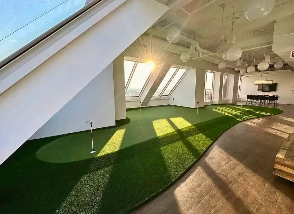 An indoor putting green running the length of a sunlit office floor