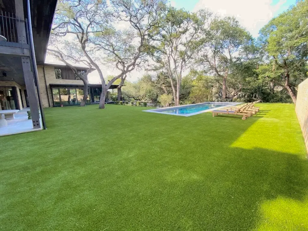 A wide synthetic lawn under oak trees, running out to a pool and loungers