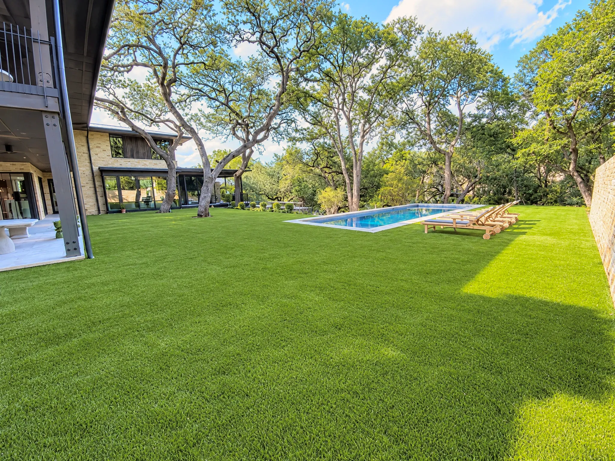 A wide synthetic lawn under oak trees, running out to a pool and loungers